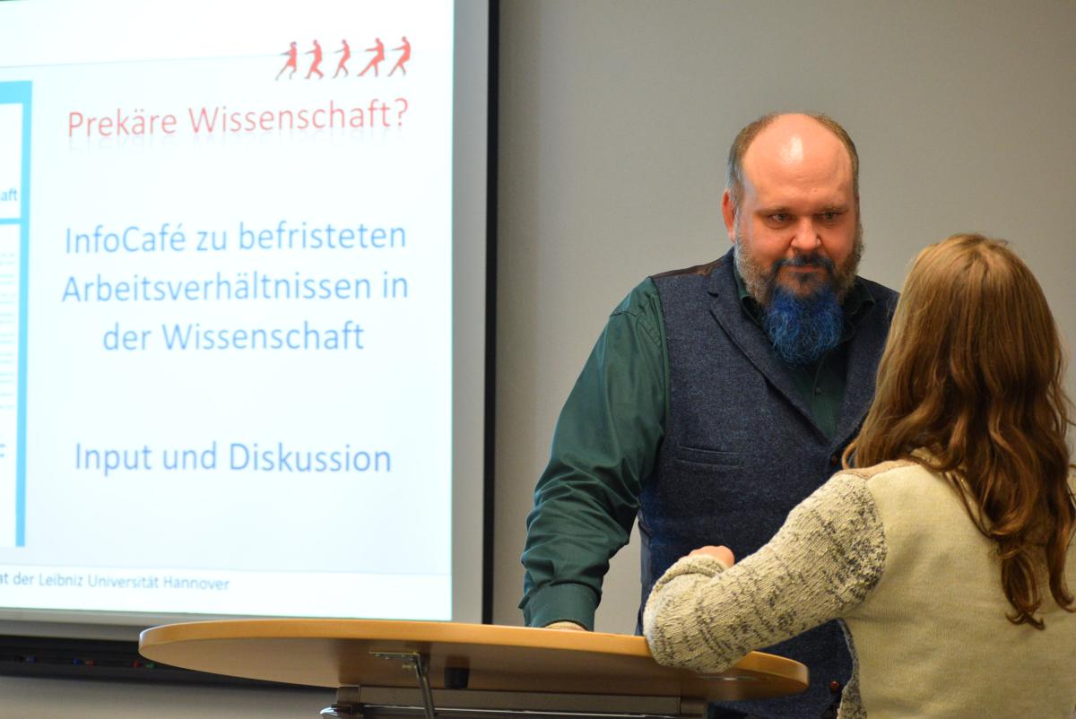 Ein Mitglied des Personalrats führt ein Beratungsgespräch mit einer Kollegin. Im Hintergrund ist eine Präsentation zu Vertragsbefristung im wissenschaftlichen Bereich zu sehen.